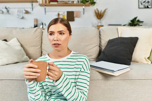 Détente dans un salon moderne, une jeune femme sirote soigneusement sa boisson chaude assise. — Photo de stock