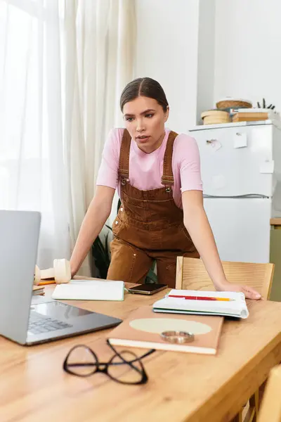 Jovem mulher em macacão elegante se envolve com seu laptop, cercado por um espaço de trabalho arrumado. — Fotografia de Stock