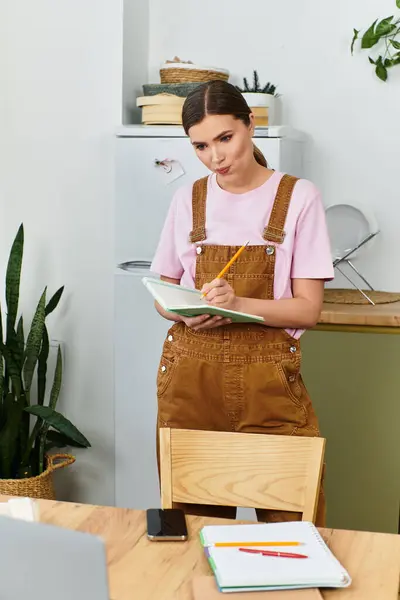 Woman stands in contemporary kitchen, focused on writing notes as she prepares a creative project. — Stock Photo