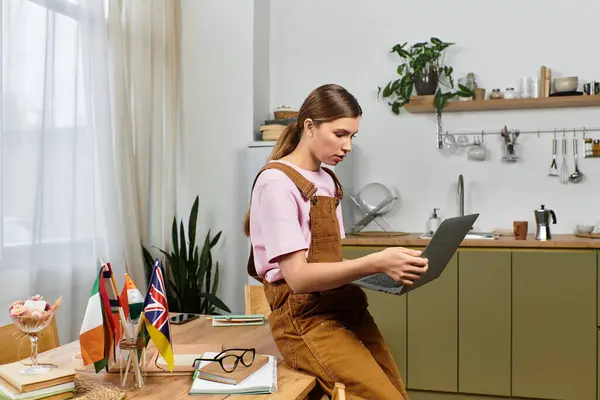 A beautiful young woman focused on her laptop while sitting on a kitchen table surrounded by flags. — Stock Photo