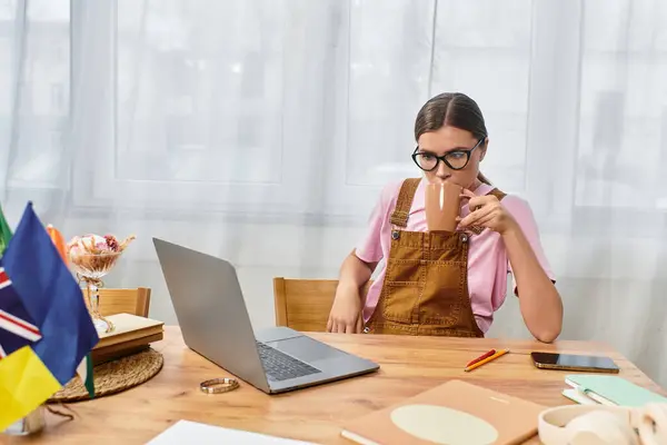 A young beautiful woman sips coffee at her desk while focused on her laptop and notes. — Stock Photo