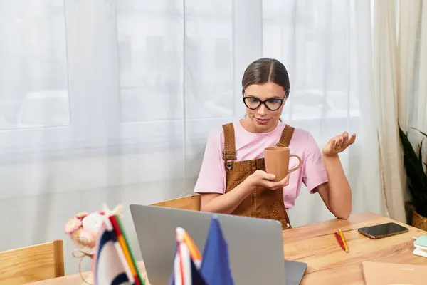 A young beautiful woman sips coffee and gestures during a lively conversation at her desk. — Stock Photo