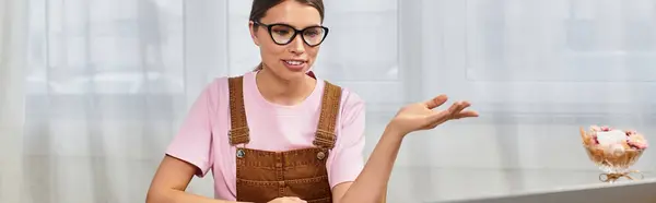 A young beautiful woman in stylish overalls chats animatedly at her desk in a bright interior. — Stock Photo