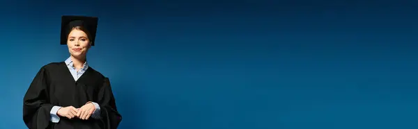 Happy graduate in cap and gown smiles confidently against a blue background. — Stock Photo