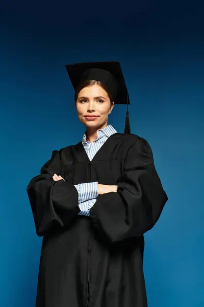 Una mujer joven se levanta orgullosamente en su vestido de graduación y gorra, mostrando su logro. - foto de stock
