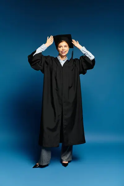 Young beautiful woman joyfully adjusts her graduation cap while smiling brightly in a studio. — Stock Photo