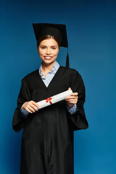 A young woman in a gown beams while proudly holding her diploma with a red ribbon. — Stock Photo