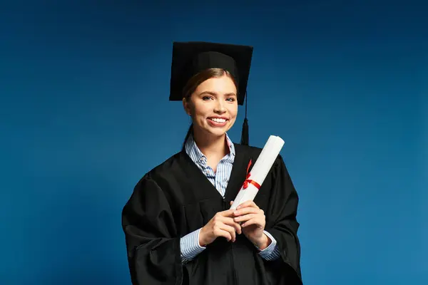 A young beautiful woman smiles brightly while holding her diploma, dressed in a graduation gown. — Stock Photo