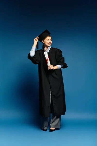 Una mujer alegre en traje de graduación se para con confianza, ajustando su gorra con una sonrisa brillante. - foto de stock