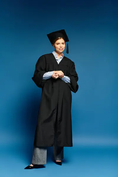 Young woman in a graduation gown and cap stands confidently, embodying success and joy. — Stock Photo