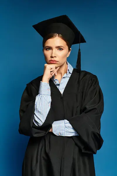 A young woman in a graduation gown poses thoughtfully against a striking blue backdrop. — Stock Photo