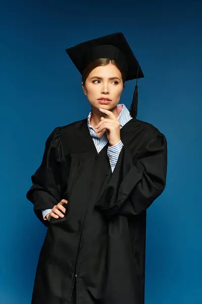Confident woman in graduation gown and cap reflects on her aspirations in a modern setting. — Stock Photo