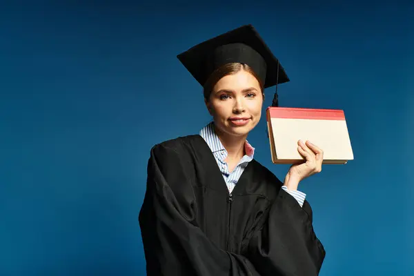 Young woman radiates joy in her graduation attire while holding a diploma against a blue backdrop. — Stock Photo