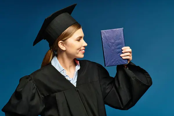 Una joven feliz en un vestido de graduación orgullosamente muestra su diploma. - foto de stock