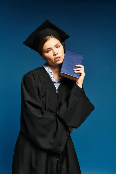Young woman in graduation attire holds a book, exuding pride and contemplation. — Stock Photo