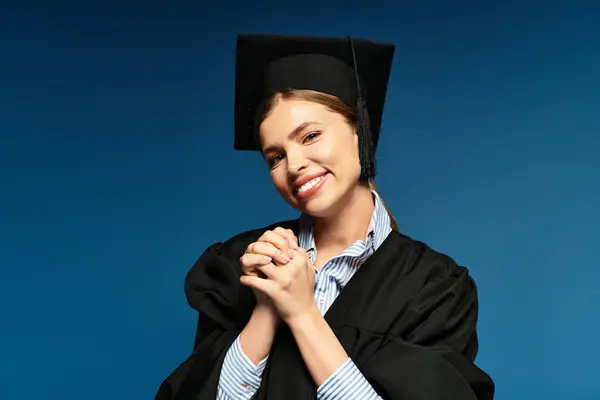 Joyful graduate in gown and cap, smiling brightly with hands clasped in excitement. — Stock Photo