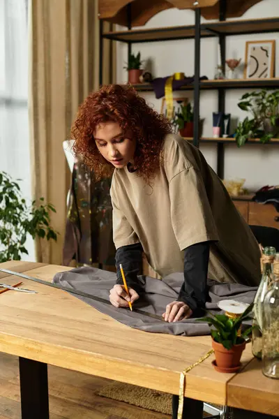 Une jeune femme talentueuse dessine méticuleusement des motifs sur tissu gris dans son élégant atelier artisanal. — Photo de stock