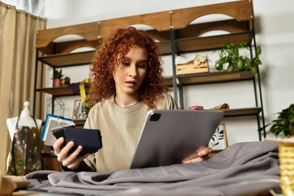 Une jeune femme talentueuse conçoit sur sa tablette, entourée de tissu et d'outils. — Photo de stock