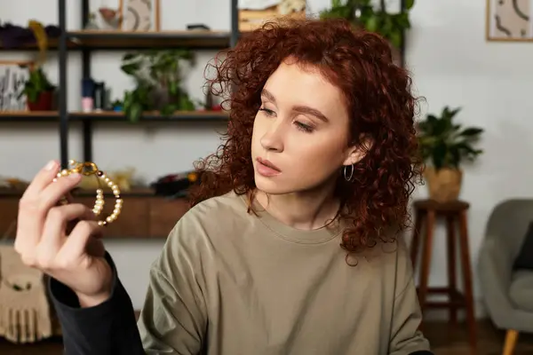 Young woman with curly red hair focuses intently on crafting a unique accessory in her cozy studio. — Stock Photo