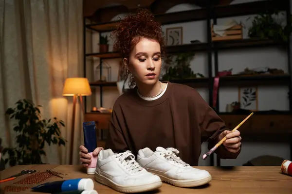 A young, beautiful woman engages in a DIY project, customizing her sneakers at a cozy workspace. — Stock Photo