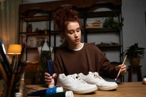 Beautiful craftswoman enhances her sneakers with paint and brushes in a stylish craft room. — Stock Photo