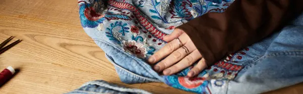 Belle jeune femme met en valeur son talent en bricolage en embellissant denim avec broderie colorée. — Photo de stock
