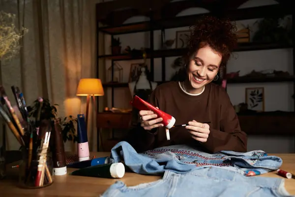 Une jeune belle femme crée des designs uniques sur le denim dans son espace de travail accueillant à la maison. — Photo de stock