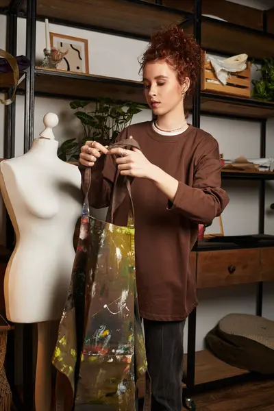 Una joven mujer hermosa se centra en su oficio, preparando su delantal en un estudio elegante y creativo. - foto de stock