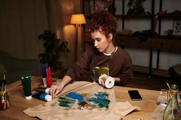 Young craftswoman painting an artistic design on fabric in her cozy workspace. — Stock Photo