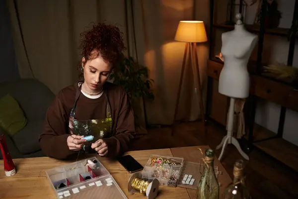 Una joven se centra en su proyecto de bricolaje, rodeada de artículos de artesanía en una cálida sala iluminada. - foto de stock