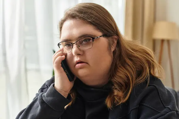 A young woman with Down syndrome confidently chats on the phone while relaxing at home. — Stock Photo