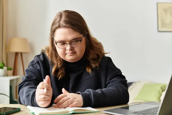 A young woman with Down syndrome engages in studying while sitting at a table in her home. — Stock Photo