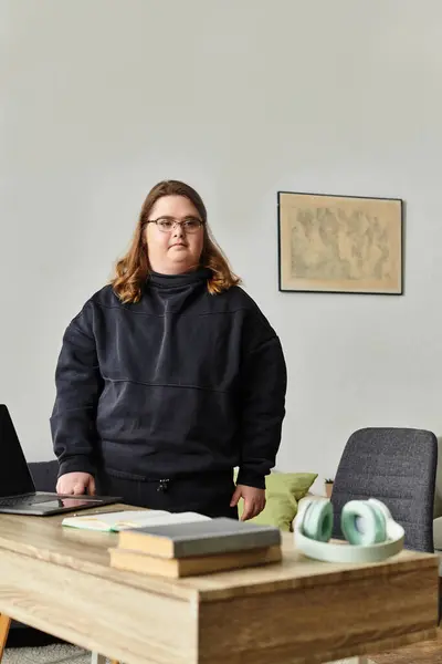 A young woman with Down syndrome stands confidently at her desk in a comfy and inviting home space. — Stock Photo