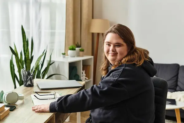 A young woman with Down syndrome sits comfortably at her home desk, exuding confidence and warmth. — Stock Photo