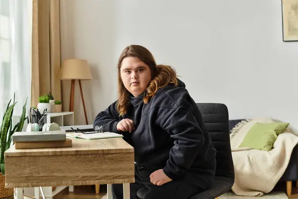 In a welcoming space, a young woman with Down syndrome embodies comfort while seated at a desk. — Stock Photo