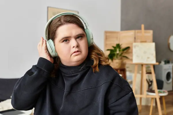 A young woman with Down syndrome relaxes at home, listening to music with headphones on. — Stock Photo