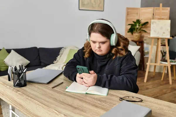 A young woman with Down syndrome sits at a desk, comfortably engaged with her phone. — Stock Photo