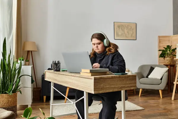 Una mujer joven con síndrome de Down trabaja diligentemente en su computadora portátil en una cómoda oficina en casa. - foto de stock