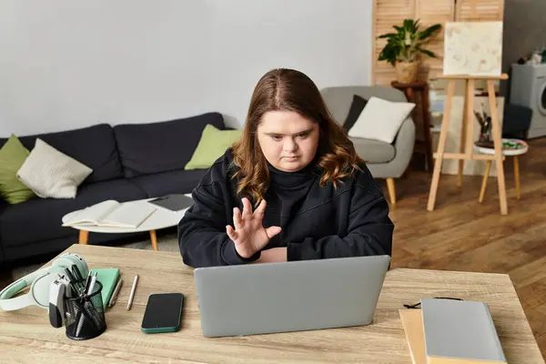 A young woman with Down syndrome focuses on her laptop while dressed in comfy attire at home. — Stock Photo