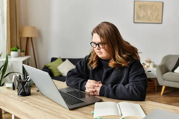 En casa, una mujer joven con síndrome de Down se centra con confianza en su computadora portátil. - foto de stock