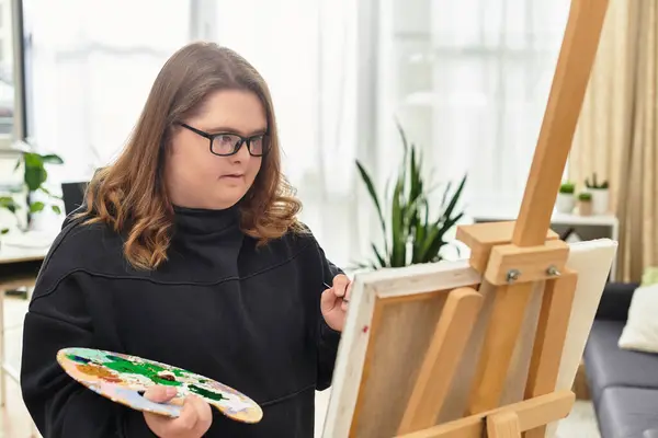 Young woman with Down syndrome enjoys painting at home, channeling her creativity in a cozy space. — Stock Photo