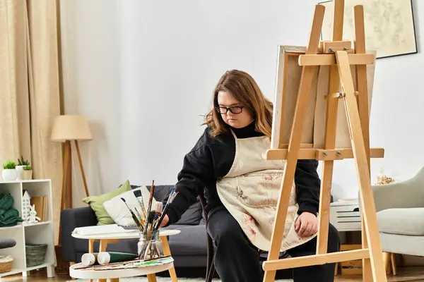 Young woman with Down syndrome paints at home, surrounded by comfort and art supplies. — Stock Photo