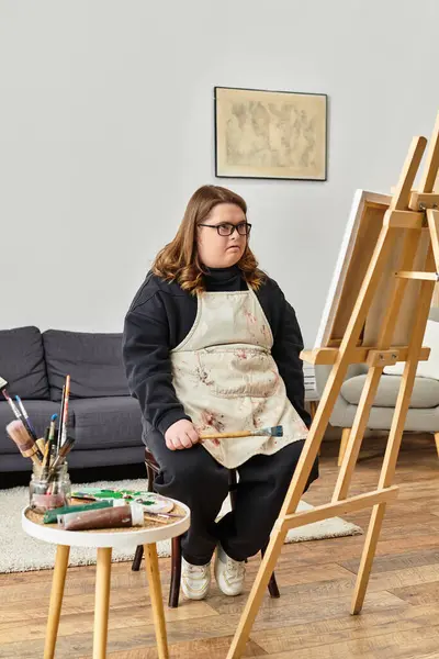 A young woman with Down syndrome sits confidently in her home studio, ready to paint on canvas. — Stock Photo