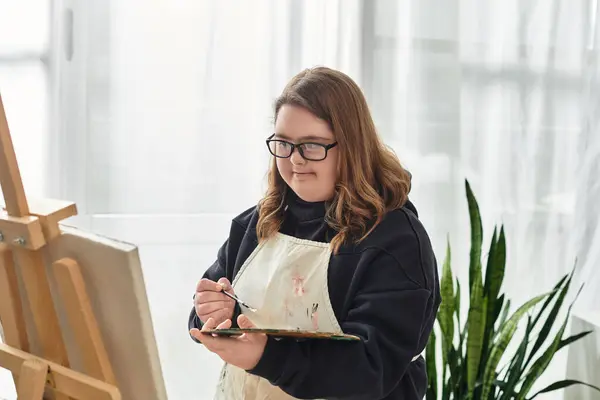 A young woman with Down syndrome expresses creativity at home, focused on her painting. — Stock Photo