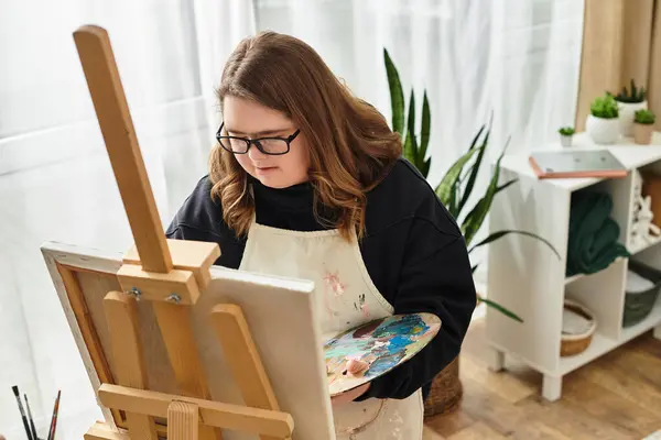 Young woman confidently paints on an easel, showcasing her creativity in a cozy home environment. — Stock Photo