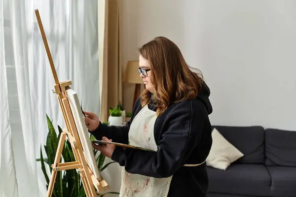 A young woman with Down syndrome paints at home, expressing her creativity and confidence. — Stock Photo