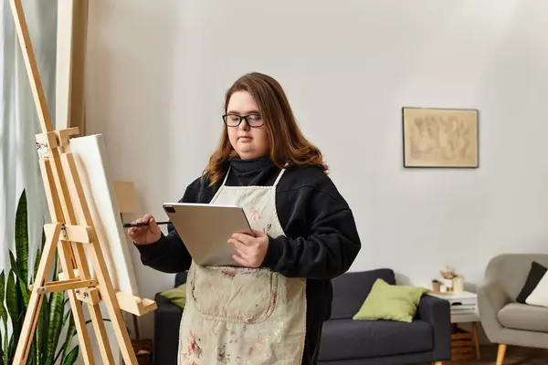 A young woman with Down syndrome stands confidently in her home studio engaged in her art. — Stock Photo