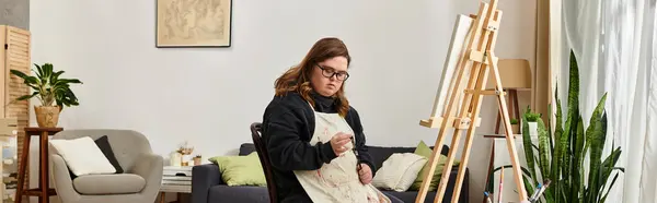 In a cozy home, a young woman with Down syndrome confidently focuses on her painting. — Stock Photo