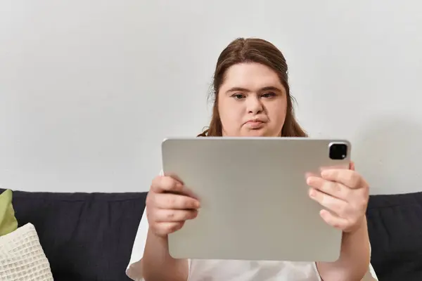 A young woman with Down syndrome relaxes at home, focused on her tablet. — Stock Photo
