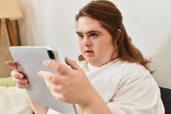 A young woman with Down syndrome sits at home, focused on her tablet and exuding confidence. — Stock Photo